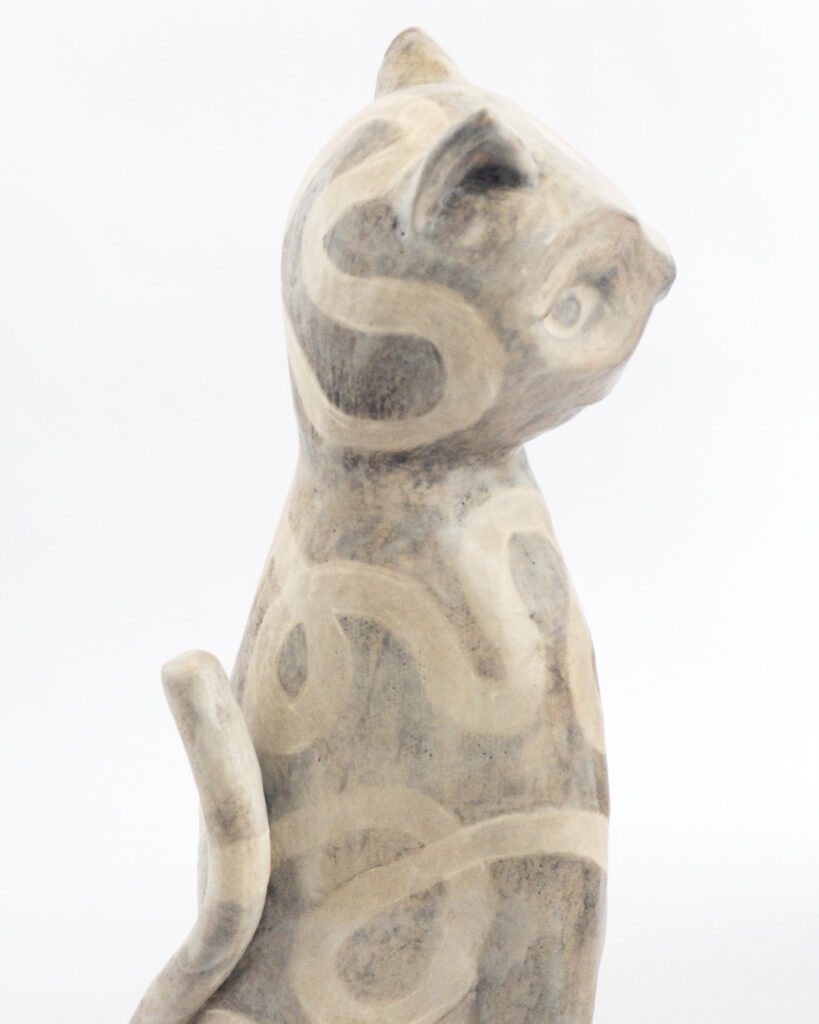 Ceramic cat glazed with a tangled swirly pattern in matte brown and beige glazes, close up from the side