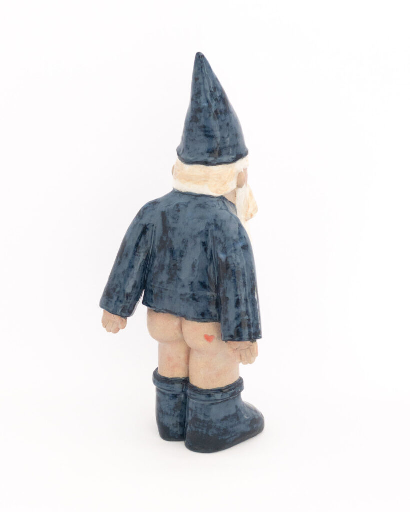 Ceramic gnome wearing blue hat, shirt and boots, but no trousers, rear view showing a heart tattoo on his bum