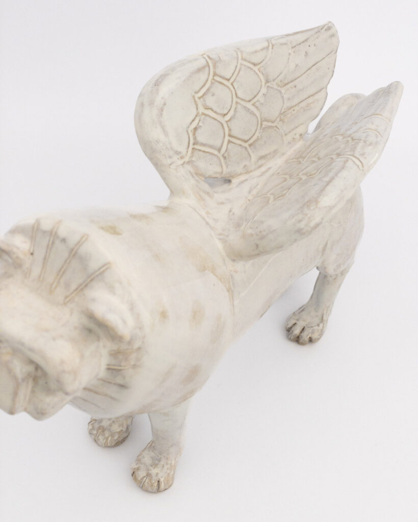 Winged ceramic lion in white glaze, showing wings from above