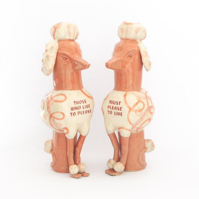 Pair of ceramic poodles in pink glazes and swirly designs with the text "Those Who Live to Please" and "Must Please to Live" on their chests