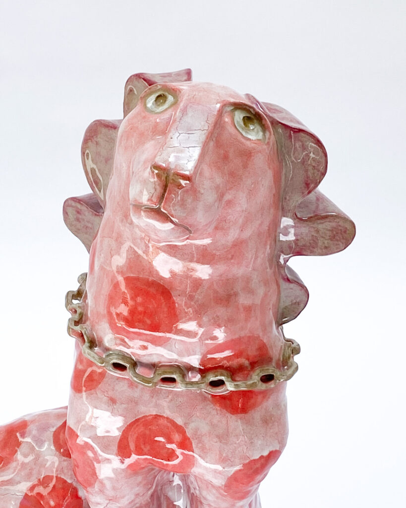 Ceramic sculpture of a quirky dog with pink glaze and darker pink spots, close up of the head
