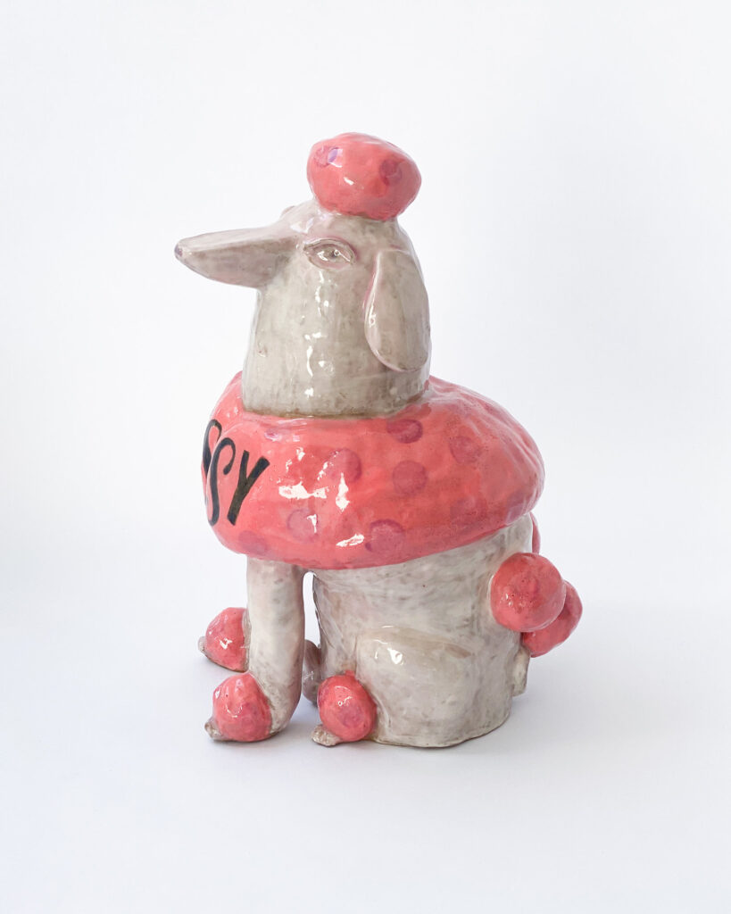 Ceramic poodle with pink fur and white skin, with Sissy written across his chest in blue letters, side view