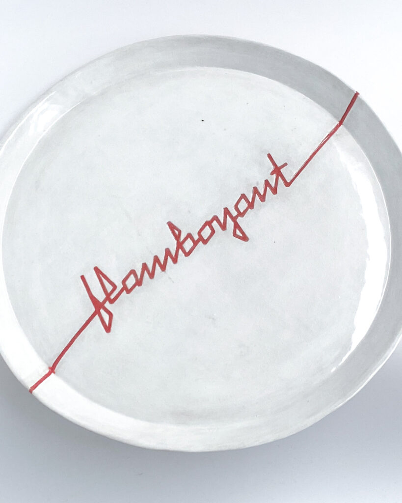 White ceramic plate with "flamboyant" carved across the surface in angular red ribbon letters