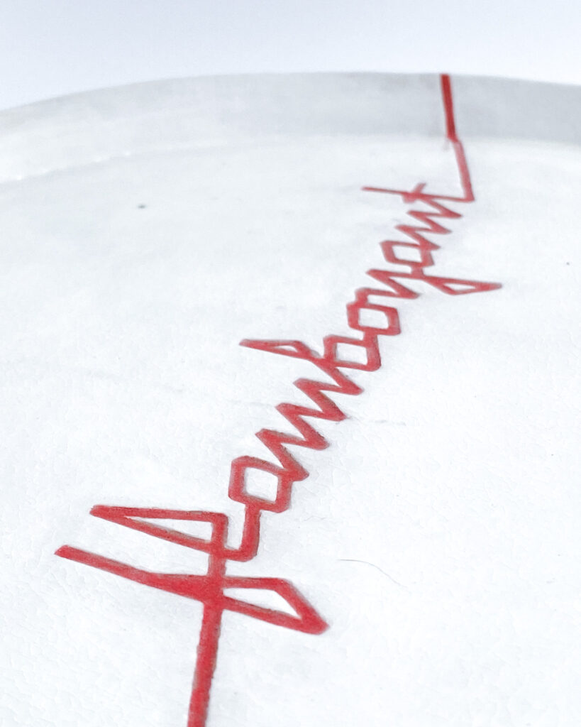 White ceramic plate with "flamboyant" carved across the surface in angular red ribbon letters, close up