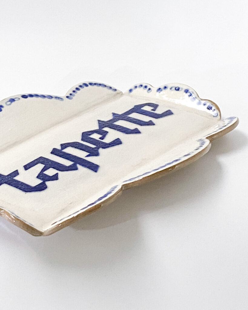 Small dish with scalloped edges and the word "tapette" written in blue blackletter writing