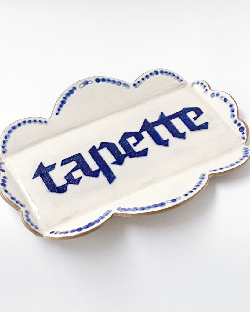 Small dish with scalloped edges and the word "tapette" written in blue blackletter writing