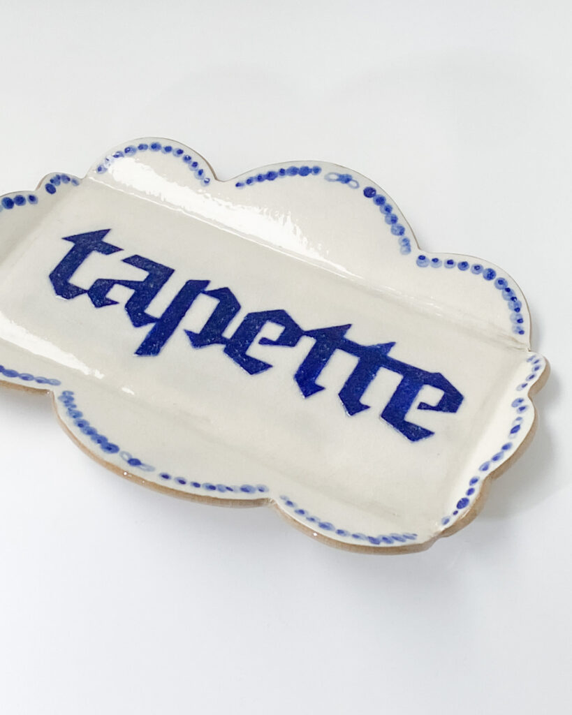 Small dish with scalloped edges and the word "tapette" written in blue blackletter writing
