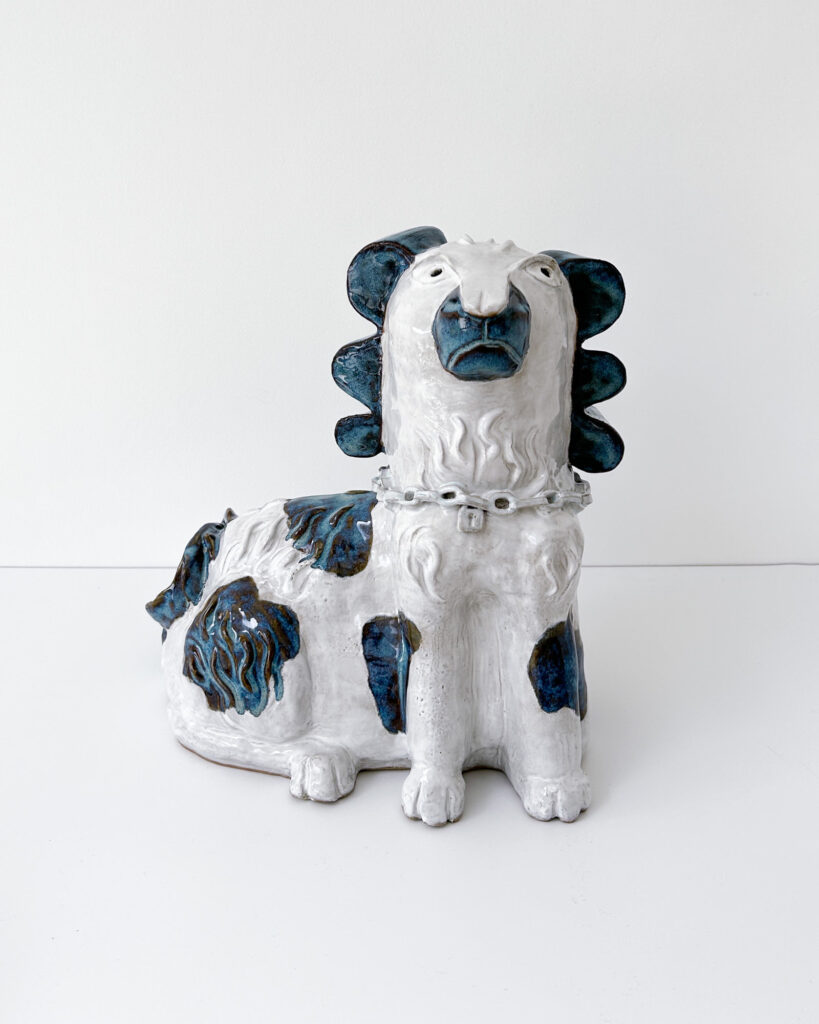 Ceramic dog in white glaze with blue and brown spots that break over the texture of his fur