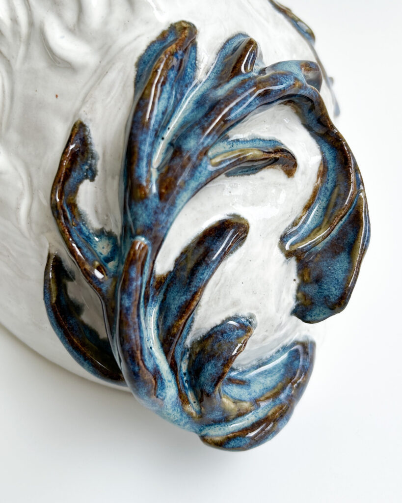 Ceramic dog in white glaze with blue and brown spots that break over the texture of his fur, close up of the tail