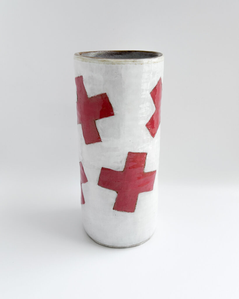 Ceramic cylindrical jar with white glaze and graphic red plus symbols scattered over the surface