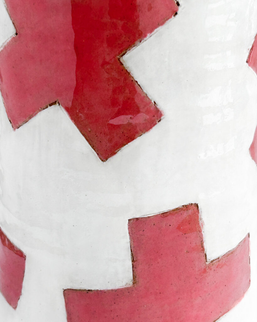 Ceramic cylindrical jar with white glaze and graphic red plus symbols scattered over the surface, close up