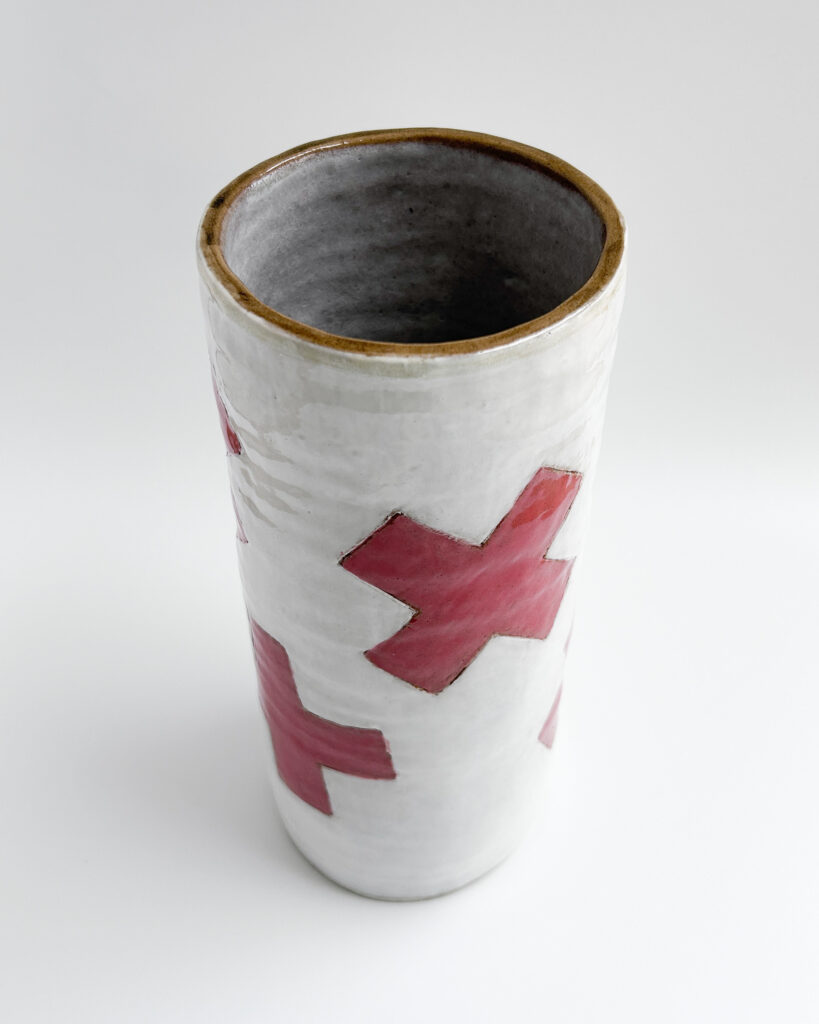 Ceramic cylindrical jar with white glaze and graphic red plus symbols scattered over the surface, looking down from above