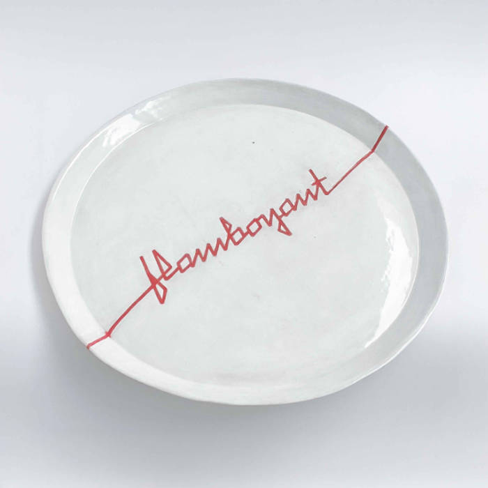 Ceramic plate glazed in white, with "Flamboyant" carved across it  in angular red ribbon letters