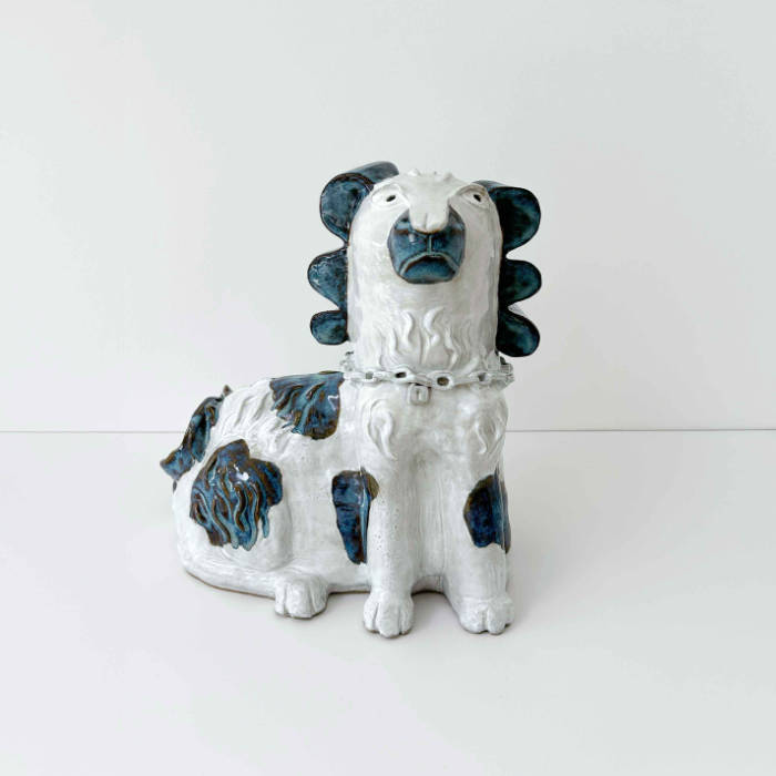 Ceramic dog in white glaze with blue and brown spots that break over the texture of his fur